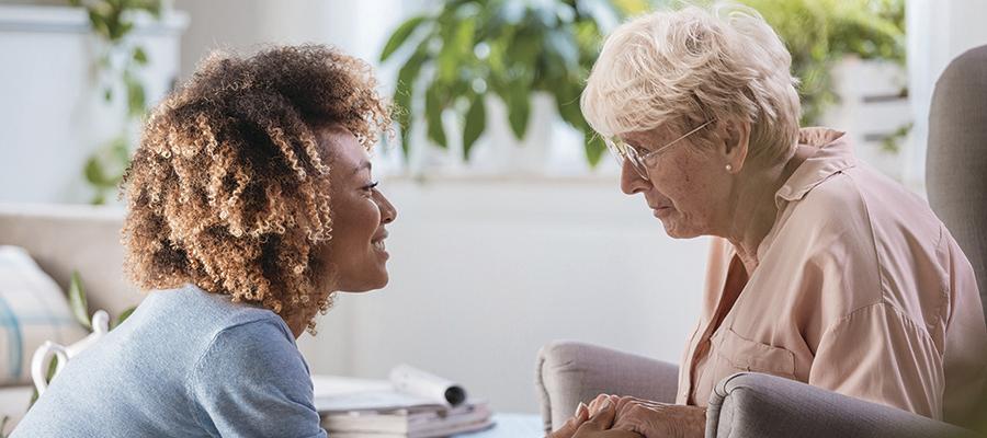 Image of young woman bending down and smiling at elderly woman in chair