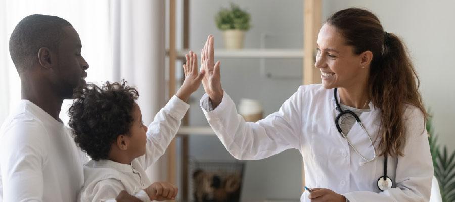 At Children’s Wisconsin in Milwaukee, Wisconsin, a father holds his son while the boy give a high-five to his doctor who is in a lab coat and has a stethoscope around her neck.