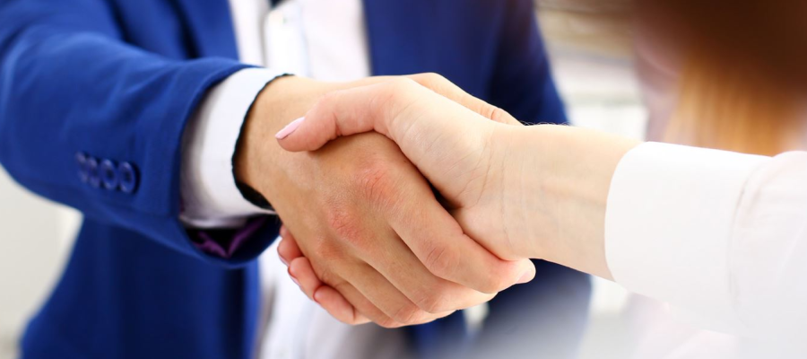 A man in a blue suit jacket and a white shirt shakes hands with a woman in a white shirt.