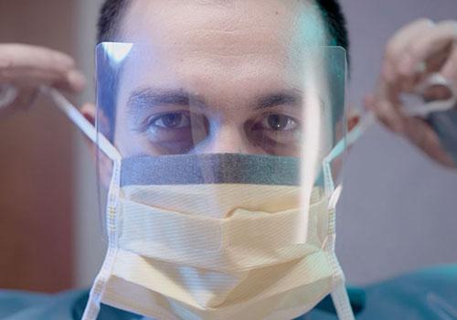 Doctor applying mask under face shield