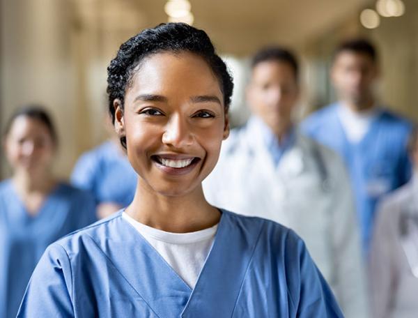 A smiling black female clincian stands in foreground with a care team behind her in background