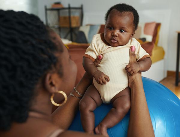 A black mother holds a baby up on a yoga ball