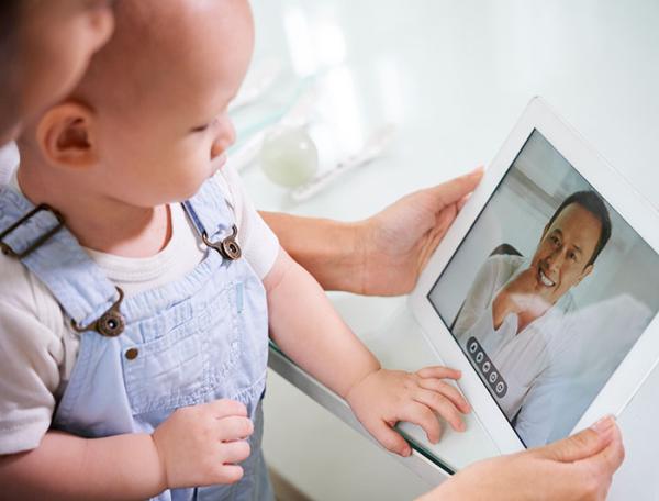 image of a mother holding a baby on her lap, with a tablet bearing a smiling clincian in virtual consult