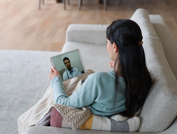 Woman seated on a sofa  views a webinar speaker on a tablet