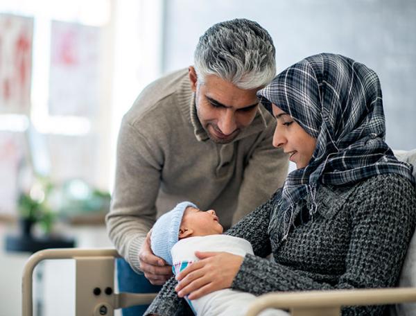 A mother in hijab and a father sit together cradling their newborn