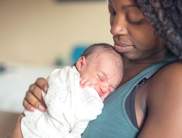 A black mother sits cradling her newborn to her chest