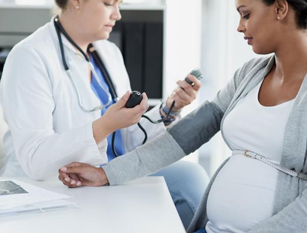 A clinician in a white coat checks a pregnant woman's blood pressure