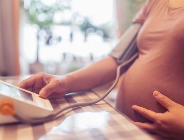 closeup of a pregnant woman's belly while she measures her blood pressure with a home device