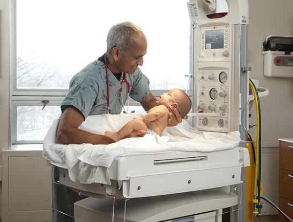 An older male clinician places a newborn on a scale