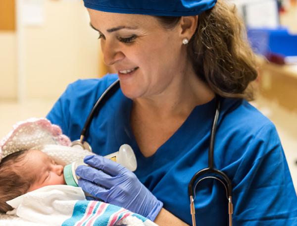 Clinician stands holding and feeding a swaddled newborn