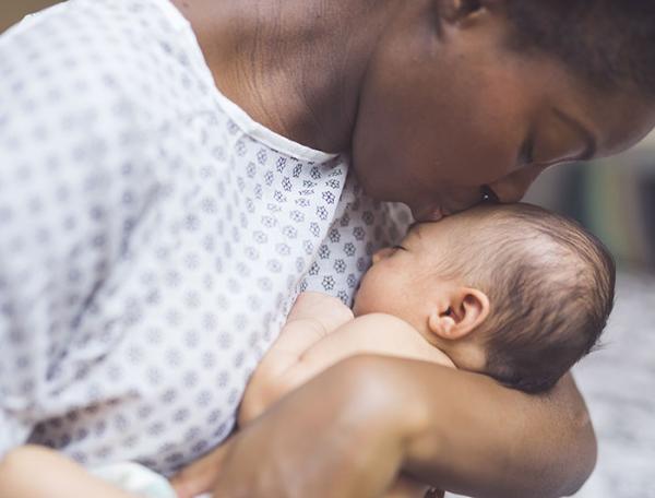 a mother in a hospital gown kisses her newborn infant's head