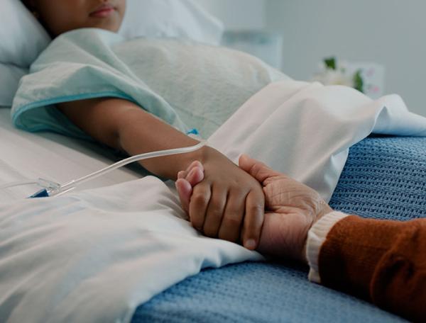 stock image of a child in a hospital bed holding a parent's hand