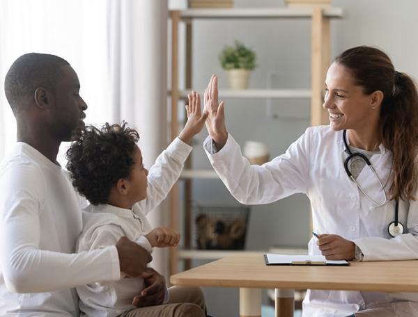 stock image of a boy sitting on his father's lap, high fiving a female doctor