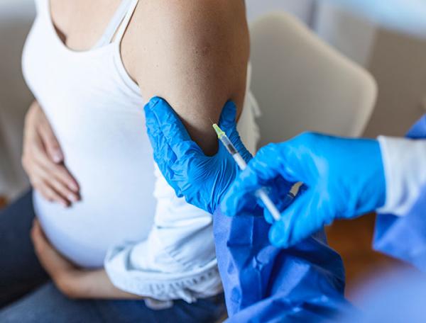 A pregnant woman gets a shot from a gloved clinician