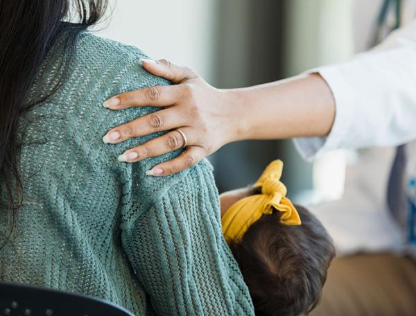 Stock image of a female hand resting on the shoulder of a mother holding an infant