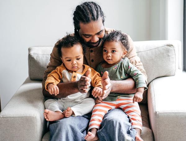 A Black father sits with two toddlers on his lap