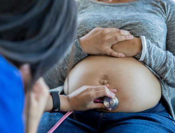 Stock image. A clinician places stethoscope on a pregnant belly to listen to fetus