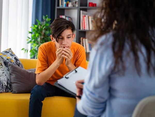 Teen boy sits on a female counselor's sofa