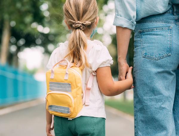 Back to school - A girl wearing a backpack walks down a street holding an adult's hand