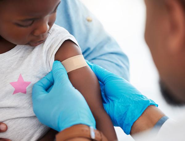 A health worker places a bandaid on a small childs bicep as the child looks on