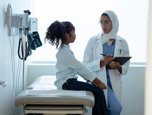 A femal doctor talks to a young girl seated on an exam table