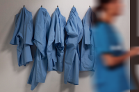 Workforce Shortages and Violence Are Rising Concerns in State of Nursing Poll. A clinician walks in front of a wall with unused scrubs handing from hooks.